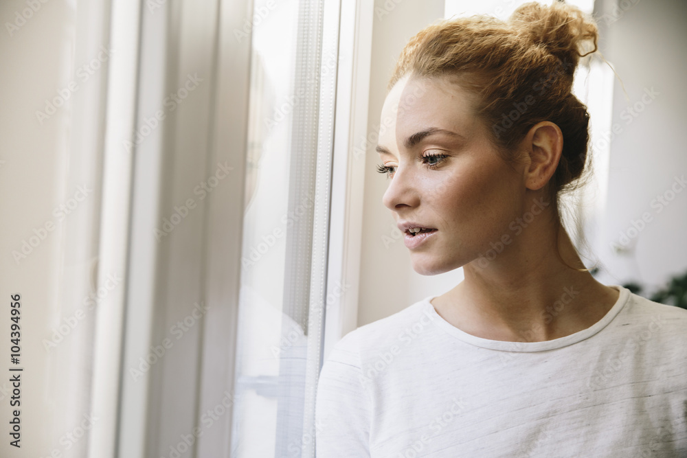 Young woman looking out of her window, being stroke by sunlight Young woman looking out of her window, being stroke by sunlight