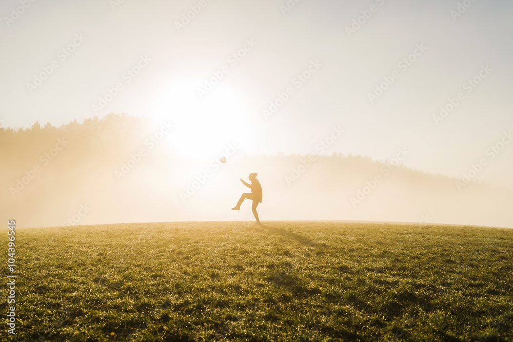 Young man playing soccer on meadow in the evening Young man playing soccer on meadow in the evening