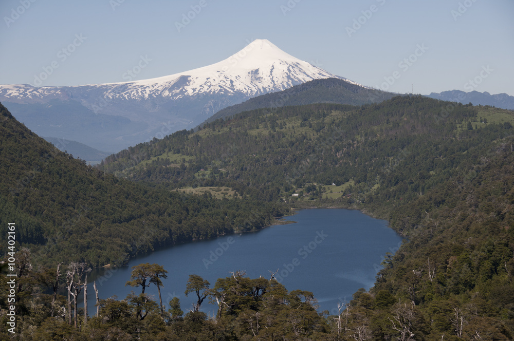 Lago y selva entre montañas con volcán Villarica nevado. Parque Nacional de Huerquehue, Chile