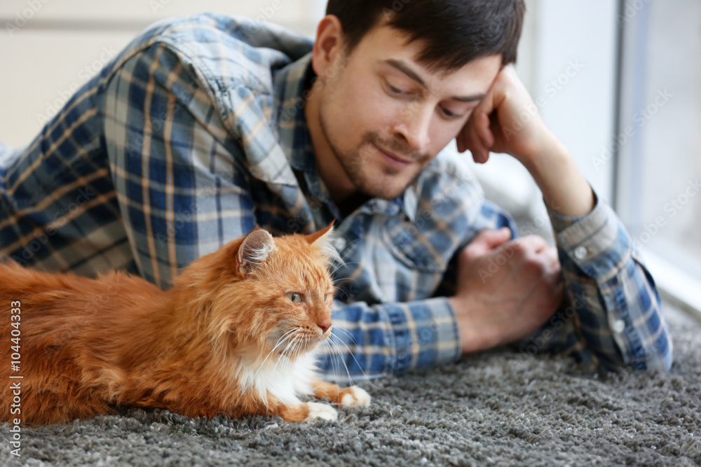 Obraz premium Young man with fluffy cat lying on a carpet