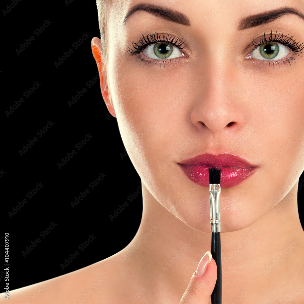 Beautiful woman paints her lips. Close-up portrait on a black background Beautiful woman paints her lips. Close-up portrait on a black background