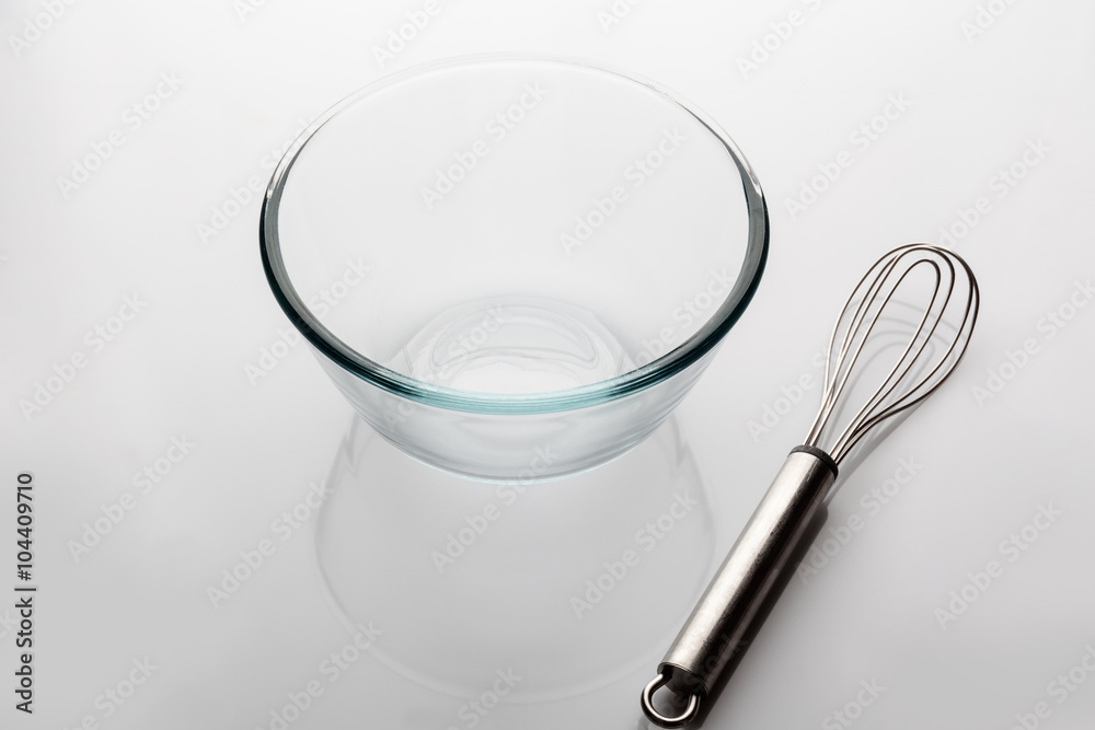 Glass transparent bowl with metal whisker aside on white background from high angle with reflection Glass transparent bowl with metal whisker aside on white background from high angle with reflection