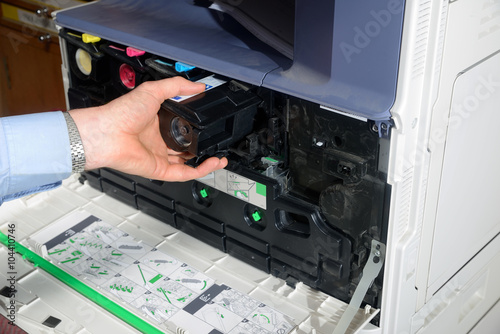 Office staff replace a toner cartridge inside the front of a photocopier