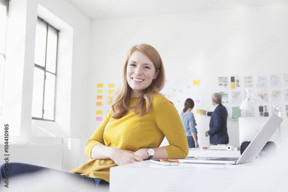 Smiling young woman in office at desk