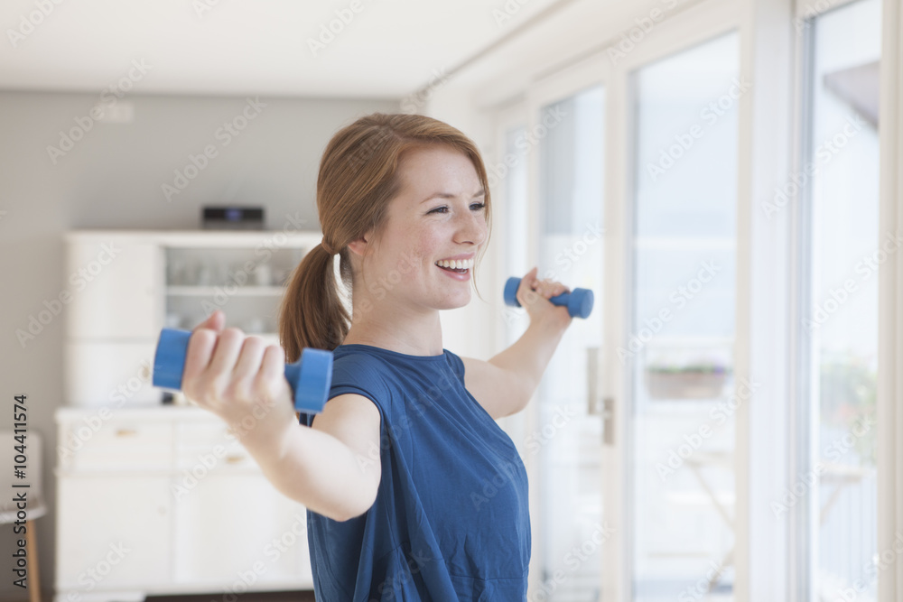 Portrait of smiling young woman exercising with dumbbells at home Portrait of smiling young woman exercising with dumbbells at home