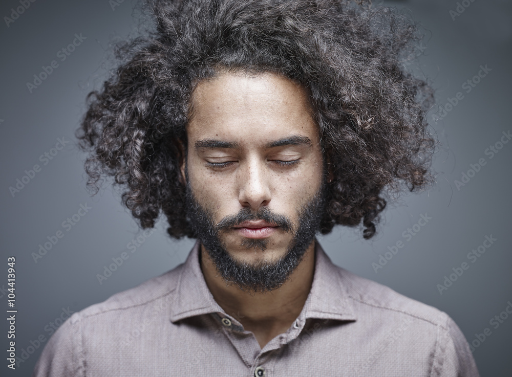 Portrait of bearded young man with curly brown hair and closed eyes in front of grey background Portrait of bearded young man with curly brown hair and closed eyes in front of grey background