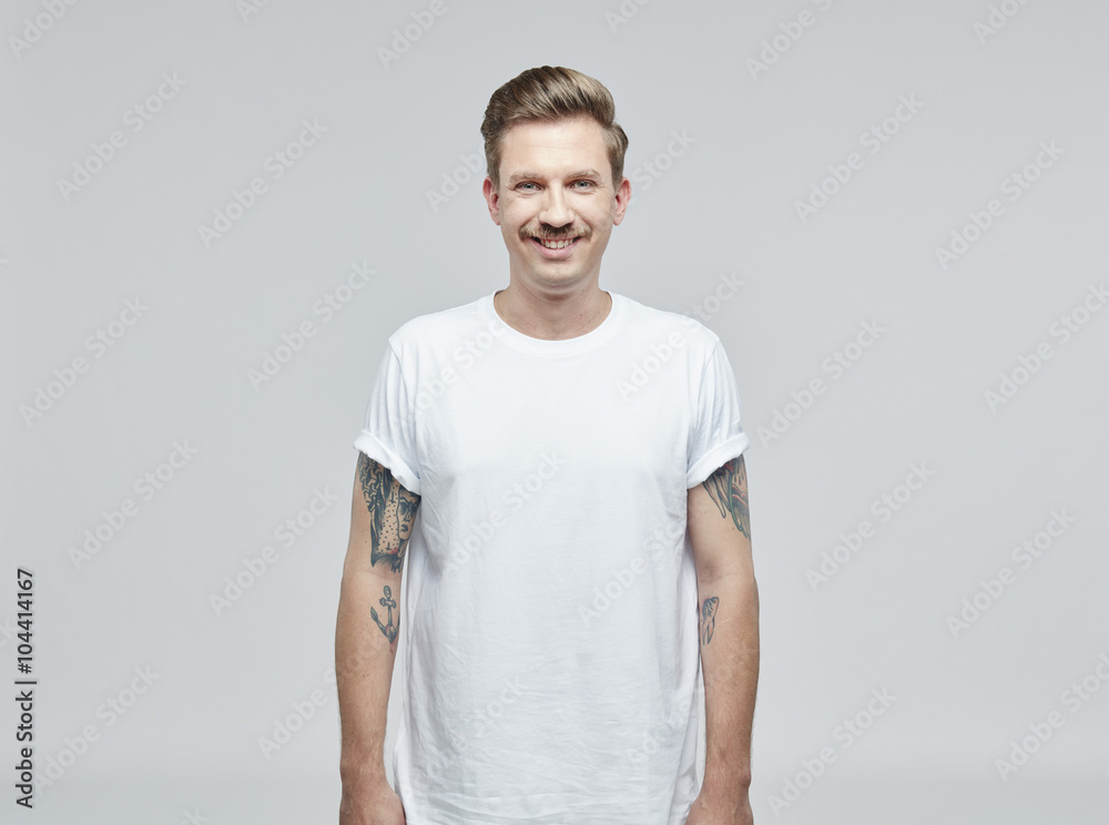 Portrait of smiling man with tattoos on his arms wearing white t- shirt in front of grey background Portrait of smiling man with tattoos on his arms wearing white t- shirt in front of grey background