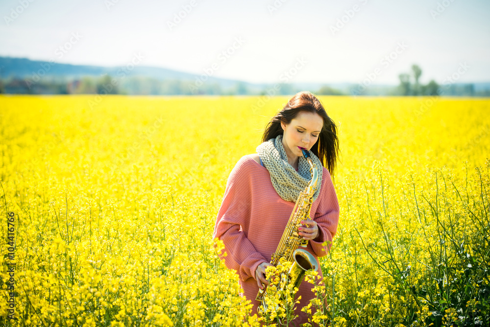 Woman playing saxophone in rapeseed field Woman playing saxophone in rapeseed field