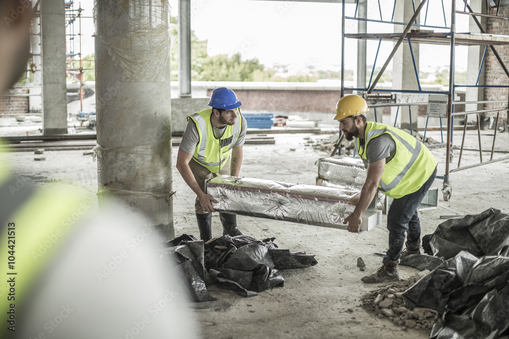 Two construction workers carrying item in construction site Two construction workers carrying item in construction site