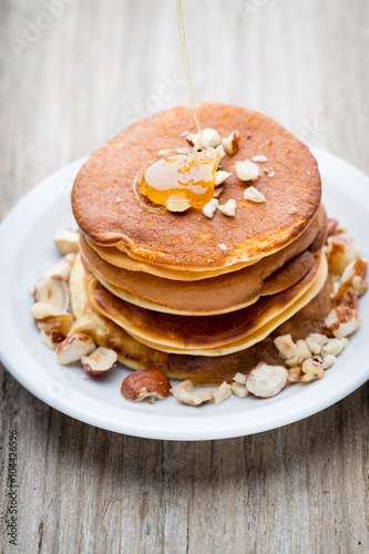 Stack of homemade pancakes with honey on wooden background.