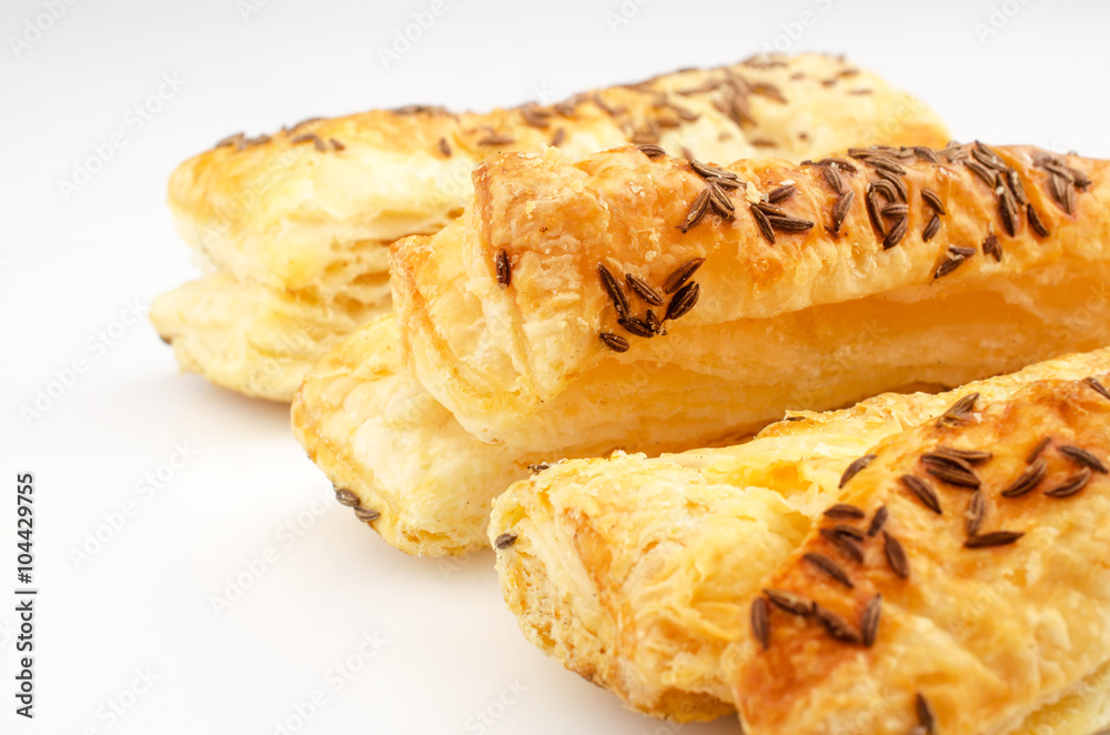Confectionery theme. Puff pastry, topped with caraway seeds, on white surface. Confectionery theme. Puff pastry, topped with caraway seeds, on white surface.