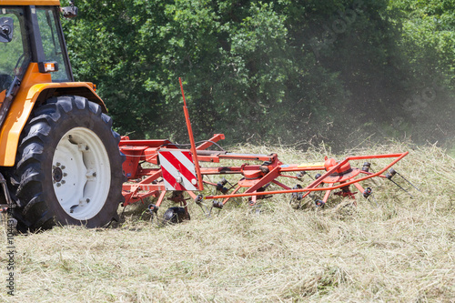 Rotary hay rake turning dried pasture grass for baling for hay to be used as winter feed for  farm livestock © gozzoli