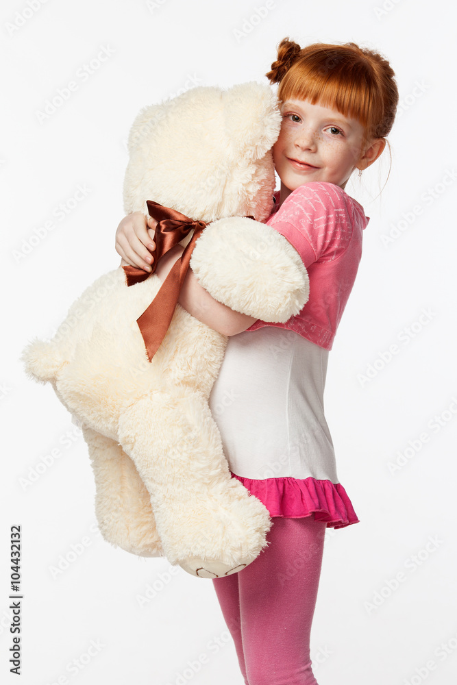 Portrait of a smiling red-haired girl in a pink shirt hugging the bear toy Portrait of a smiling red-haired girl in a pink shirt hugging the bear toy