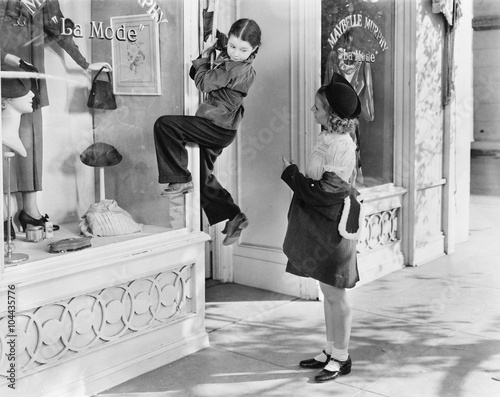 Two girls on the street with one climbing on a display window  photo