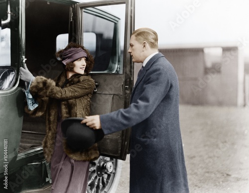 Profile of a man helping a young woman board a car 