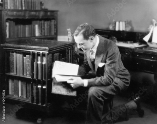 Man kneeling in his home library browsing a book 