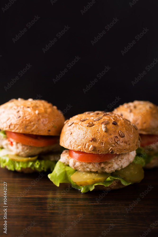 Three burgers, potatoes rustic, tomato on a dark wooden table Three burgers, potatoes rustic, tomato on a dark wooden table