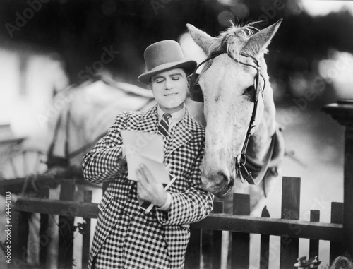 Man leaning against a fence reading a letter to his horse  photo