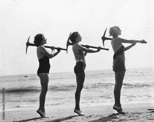 Three women posing with a pick ax on the beach 