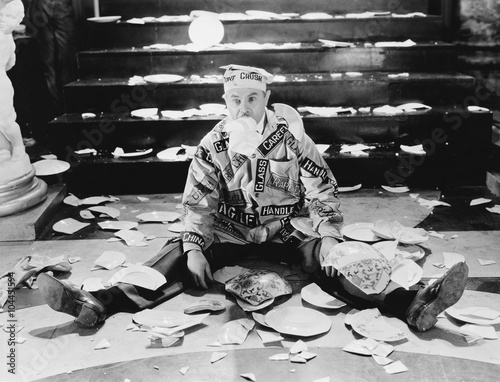 Man sitting in front of a staircase with broken plates around him 