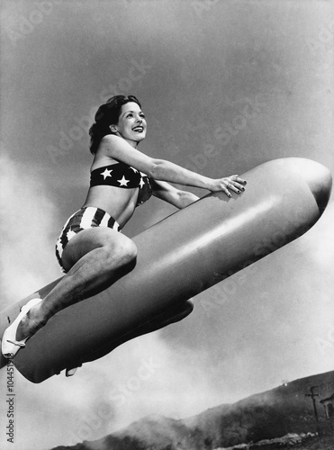 Low angle view of a young woman sitting on a rocket and smiling  photo