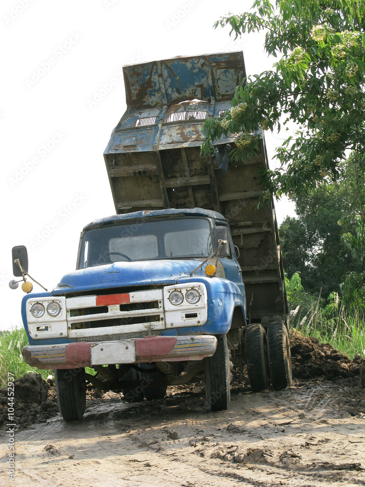 Old blue dump truck is dumping soil