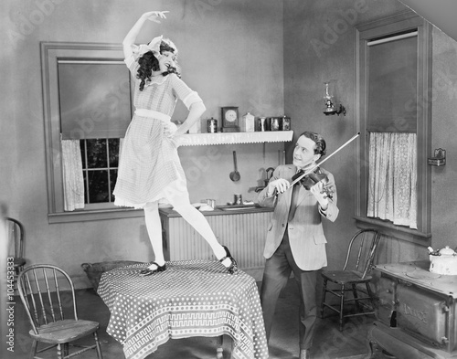 Man playing violin for woman dancing on table 