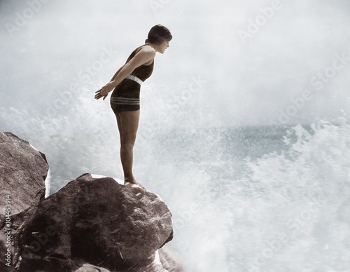 Female swimmer on rock above crashing surf   photo