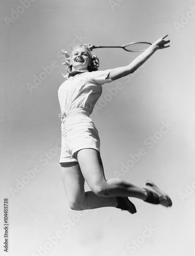 Woman jumping into the air with a tennis racket in her hand  © everettovrk