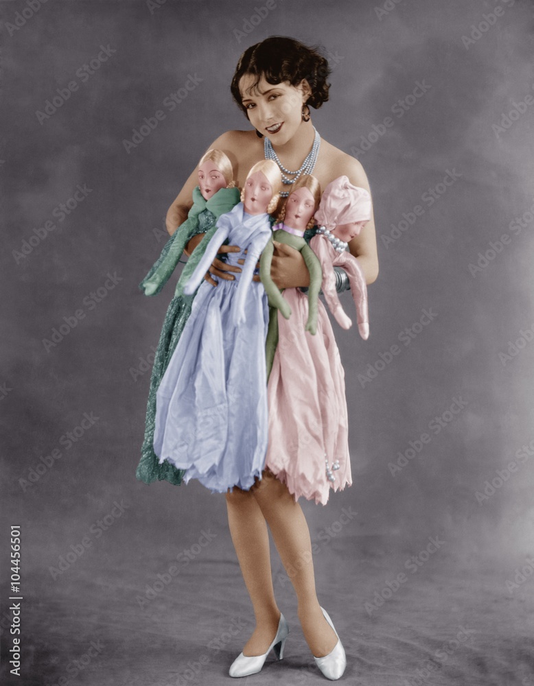 Portrait of young woman holding four dolls  