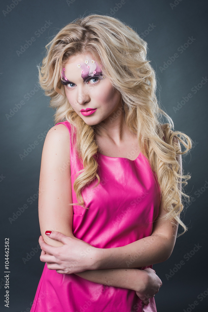 Naklejka premium sexy blonde girl with art makeup posing in the studio on a dark background wall. Pink image. Makeup with flowers.