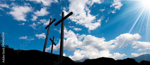 Crosses Silhouette against Blue Sky / Silhouette of three crosses against a blue sky with clouds and sun rays. Carisolo Trentino Italy photo