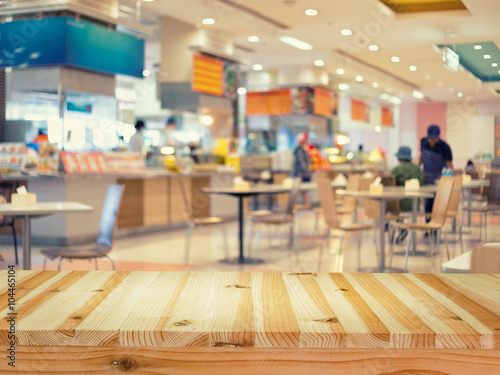 Food court or foodcourt interior blurred background. Restaurant or canteen with table, people at indoor plaza, mall, store or shopping center. Include empty wooden counter or desk for product display.