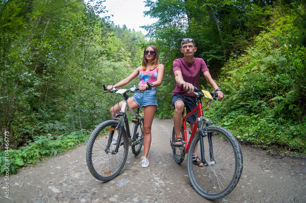 happy couple stays on a mountain road in the woods on bikes looking way
