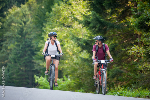 happy couple goes on a mountain asphalt road in the forest on bikes with helmets