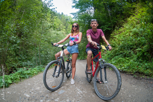 happy couple stays on a mountain road in the woods on bikes looking way