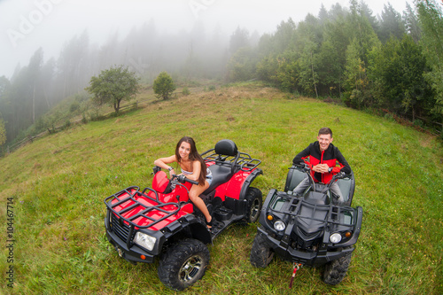 Happy beautiful couple sitting on four-wheelers ATV in foggy nature. Smiling and looking to the camera. Wide view from high piont