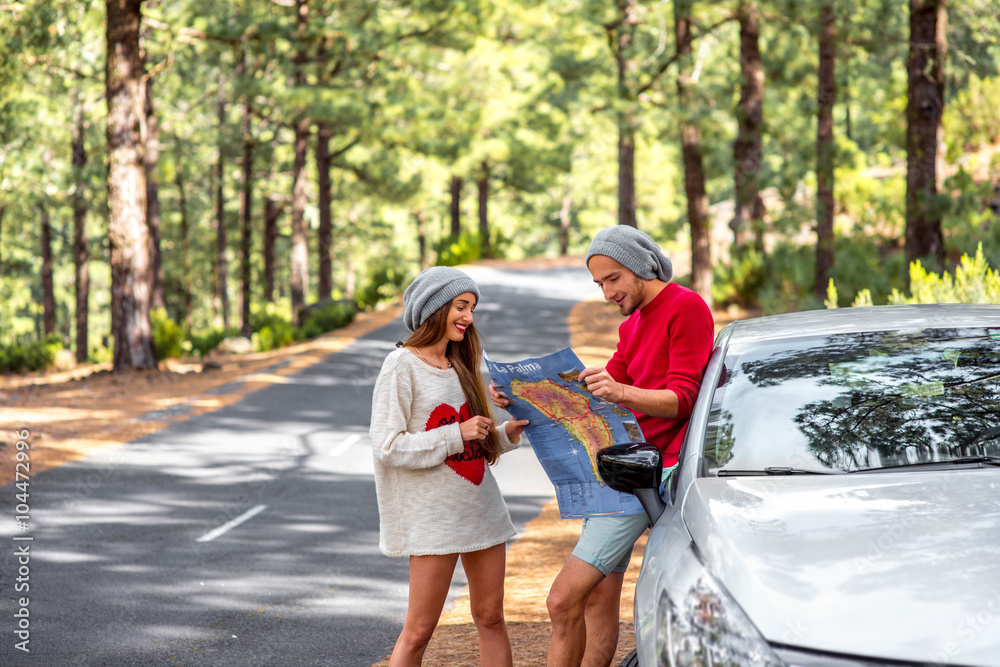 Young family in sweaters and hats holding paper map traveling La Palma island by rented car in the forest Young family in sweaters and hats holding paper map traveling La Palma island by rented car in the forest