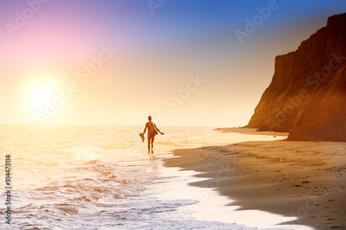Silhouette of a man retreating to the horizon on a deserted beach. Coastline, sea, high cliffs. Sunlight. 