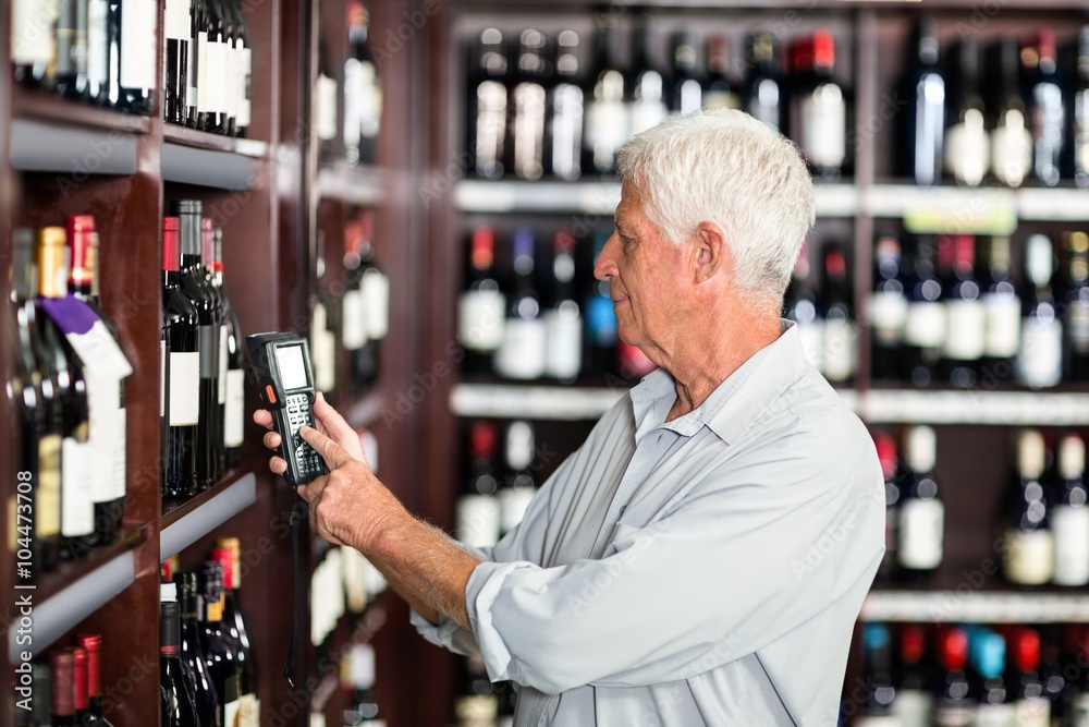 Smiling senior man scanning wine bottles at the supermarket