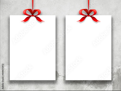Close-up of two hanged paper sheets with red ribbons weathered wall background