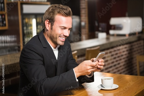 Handsome man looking at smartphone and having a coffee