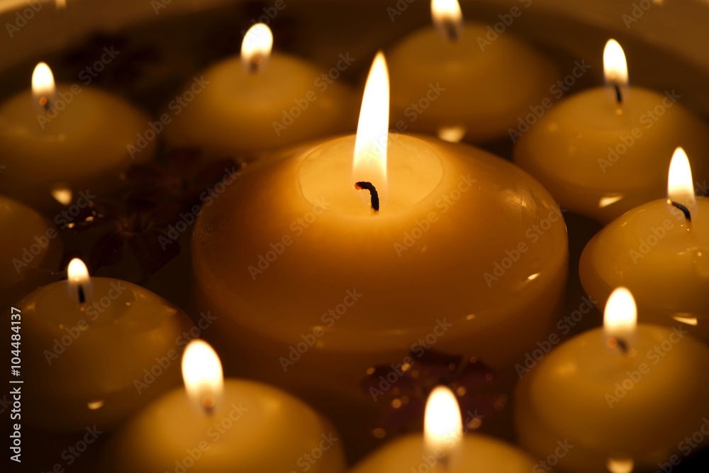 Numerous burning candles with several flowers in water, big candle in the middle