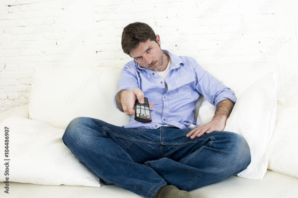 man watching television at home living room sofa with remote control looking very interested man watching television at home living room sofa with remote control looking very interested