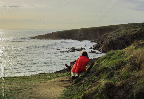 Frau blickt im Winter auf das Meer in der Abendsonne an der Küste bei Doelan in der Bretagne 