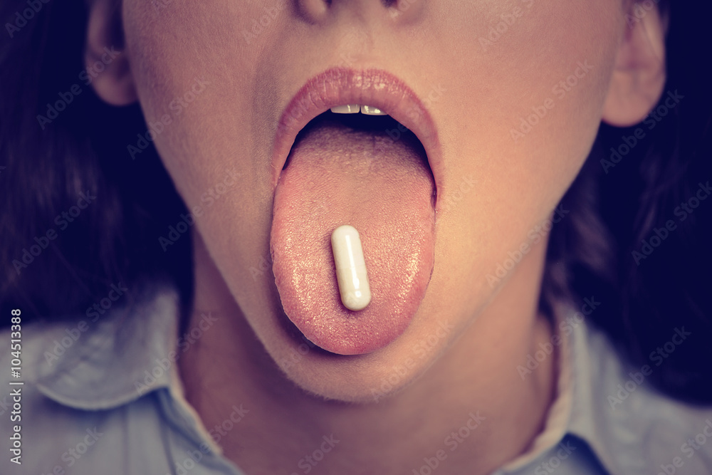Naklejka premium Closeup cropped image of young woman with white pill on her tongue