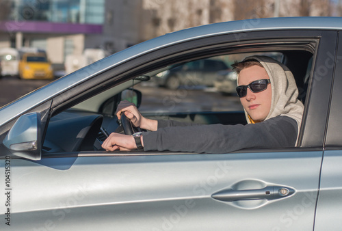 A young man in dark glasses driving a car. © sachkov