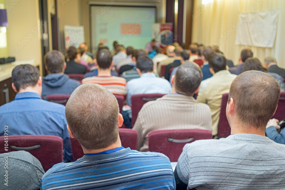 Rear view of adult students sitting and listening in lecture hall