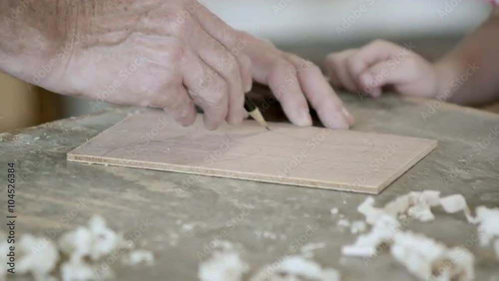 Tight shot of a grandfather drawing lines on a piece of wood, while grandson watches. Tight shot of a grandfather drawing lines on a piece of wood, while grandson watches.