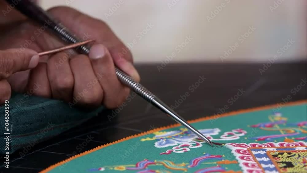 Tight shot from the side of a man carefully adding sand to a colorful sand mandala.